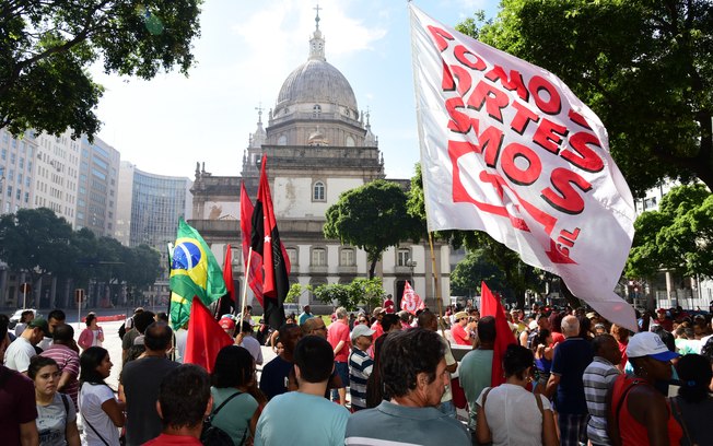 Manifestantes seguram cartazes e faixas diante da igreja da Candelrária