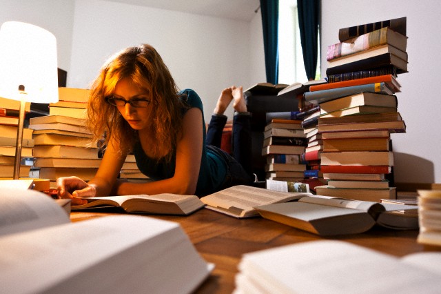 Young female lying on floor in living room and reading book